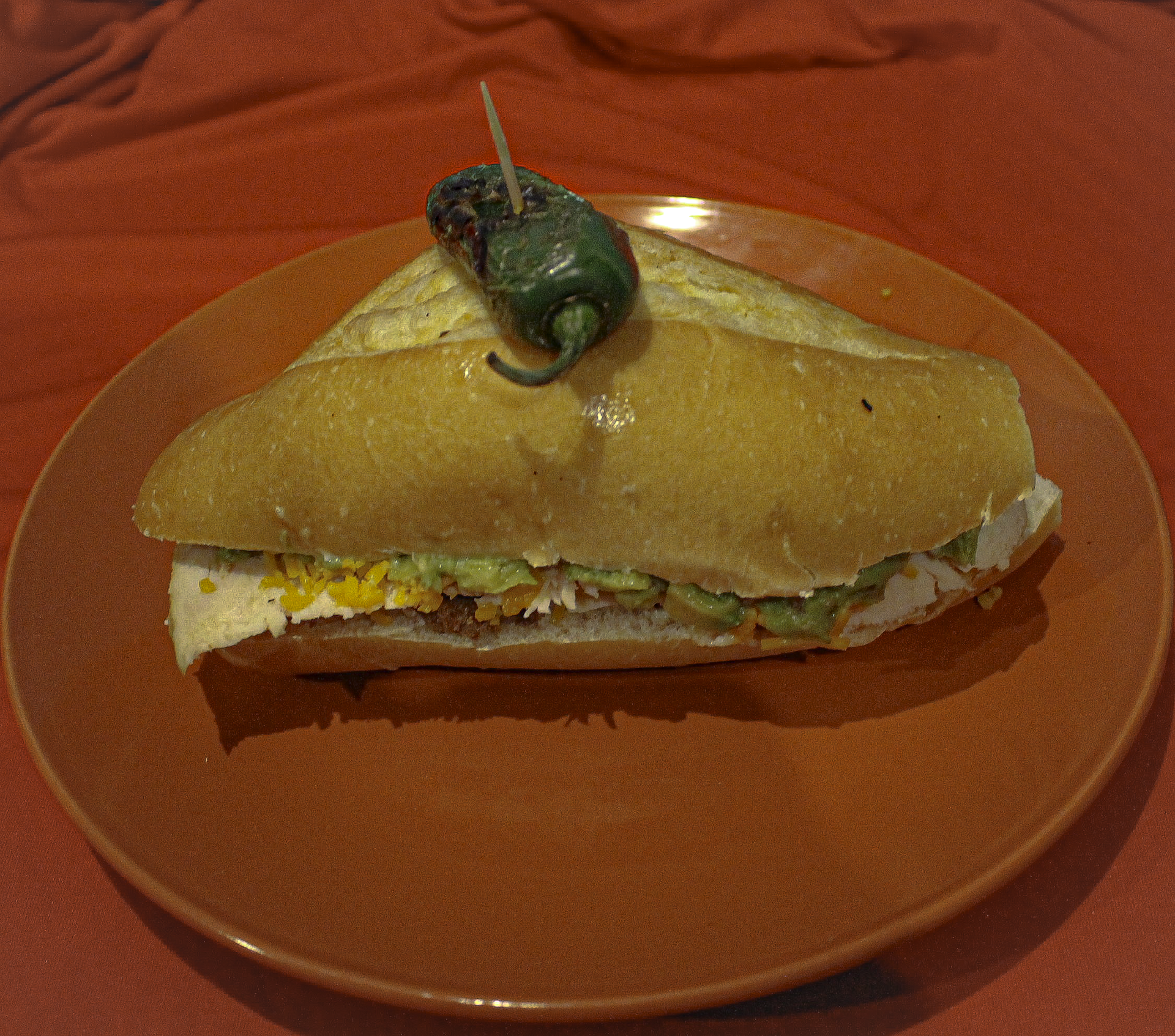 Chicken torta with guacamole, cheese, and a jalapeño on top
